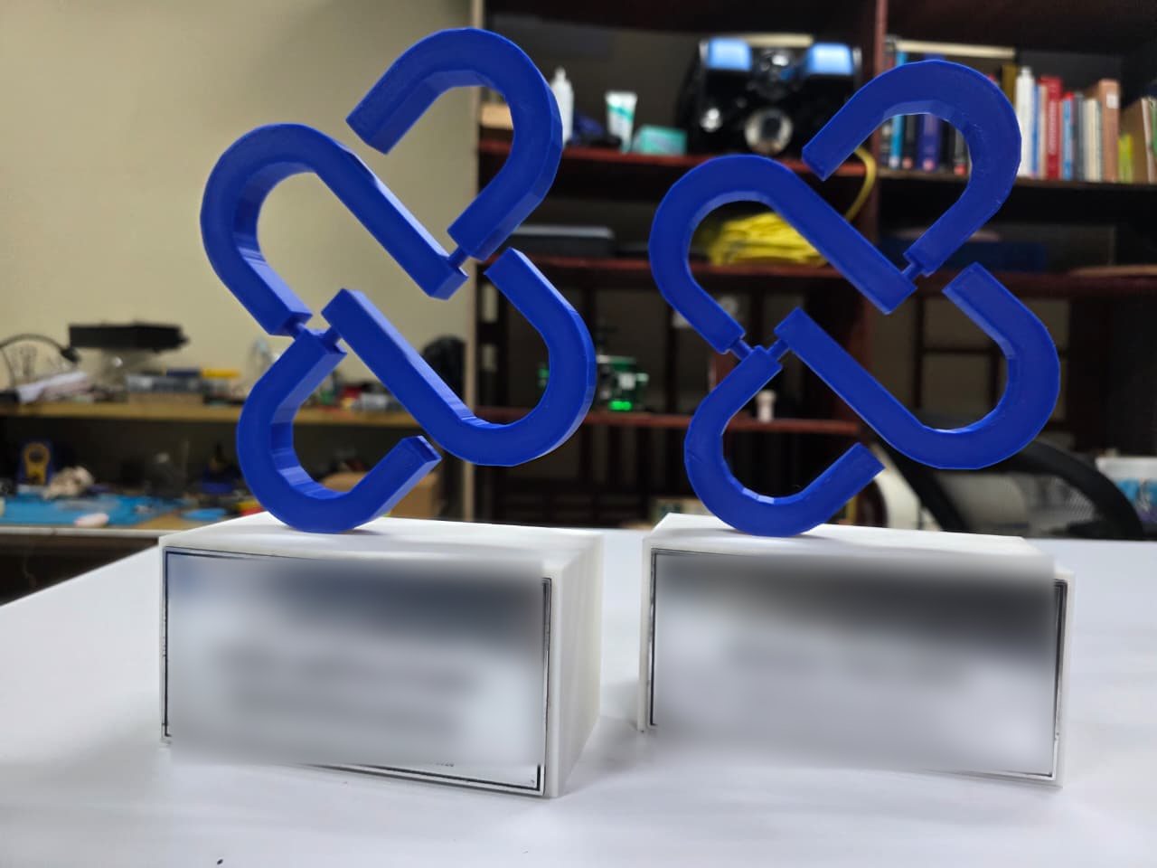 Dos trofeos impresos en 3D en azul sobre base blanca con placa grabada